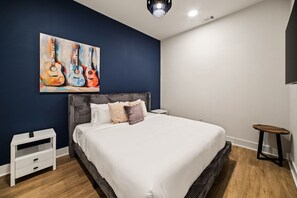 A bedroom with a bed, a nightstand, a chair, and a painting of guitars on the wall. - Good Vibes on Main | A+ Location | 1 mi to DTNash (Nashville)