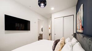 A modern bedroom with a large bed, a mounted TV, a wardrobe, and a painting on the wall.