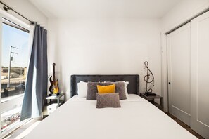 Une chambre d’hôtel avec un lit, une guitare, une petite table et une vue sur l’extérieur.