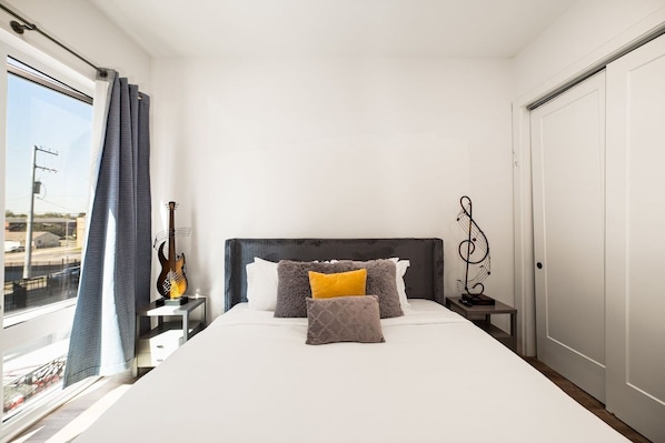 A hotel room with a bed, a guitar, a small table, and a view of the outside.