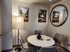 Ein moderner Essbereich mit einem runden Tisch, grauen Stühlen, einer Stehlampe und zwei gerahmten Bildern an der Wand.