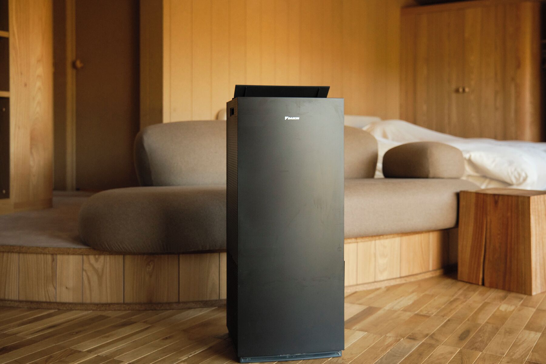 Une chambre moderne au design minimaliste, dotée d’un plancher en bois, d’un canapé avec des coussins et d’une grande armoire de couleur sombre.