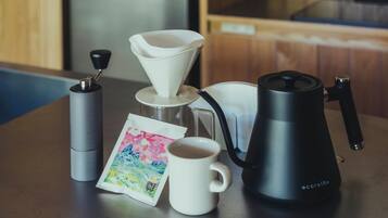 A coffee maker, a white mug, a silver container, and a colorful card on a wooden table.