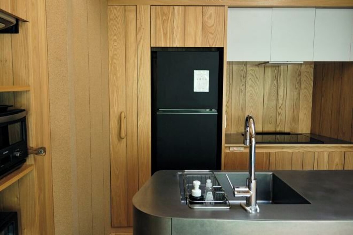 Una cocina compacta con armarios de madera, un refrigerador negro, un lavamanos de acero inoxidable y un microondas.