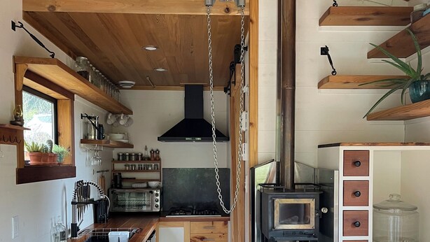 A compact kitchen with wooden cabinetry, a central island, and a wood-burning stove. - Tiny house with private hot tub (Ucluelet)