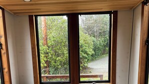 A cozy room with a blue sofa, wooden cabinets, and large windows offering a view of greenery. - Tiny house with private hot tub (Ucluelet)