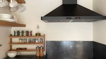 A kitchen with a black range hood, a built-in oven, and a gas stove. There are shelves with jars and a toaster oven.