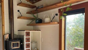 A compact kitchen with a wood-burning stove, built-in cabinets, and a window overlooking greenery. - Tiny house with private hot tub (Ucluelet)