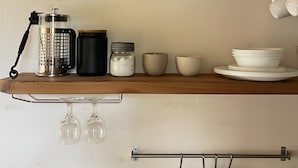 A kitchen with a wooden shelf holding glass jars of spices, a coffee maker, and a hanging knife rack. - Tiny house with private hot tub (Ucluelet)
