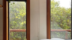 A bedroom with a large window, a wooden desk, a potted plant, and a bed with a rolled-up blanket. - Tiny house with private hot tub (Ucluelet)