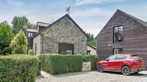 A modern house with a stone facade and a wooden extension, a red car parked in front, and a well-maintained hedge. - 2 bedroom accommodation in Ivybridge (Ivybridge)