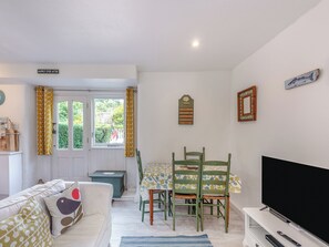 Una sala de estar acogedora con un sofá, una mesa de comedor con sillas, un televisor de pantalla plana y un mueble bajo.