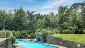 A swimming pool with a stone wall, a stone archway, and a grassy area with trees. - 2 bedroom accommodation in Ivybridge (Ivybridge)