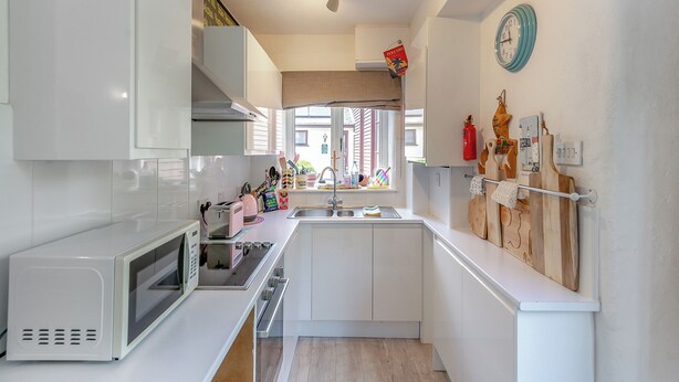 A modern kitchen with white cabinets, a microwave, a sink, and a wooden cutting board hanging on the wall. - 2 bedroom accommodation in Ivybridge (Ivybridge)