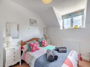 A bedroom with a wooden bed, white bedside tables, a window with a view, and a ceiling light.