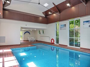 Ein Hallenbad mit gefliestem Boden, einem Rettungsring und Blick auf Grünflächen durch große Fenster.