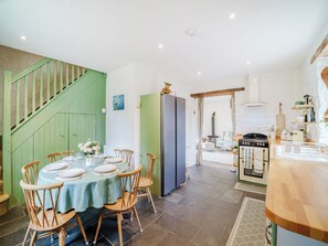 A dining area with a table set for four, a green staircase, a kitchen with a stove and sink, and a view into another room.