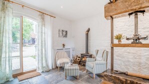 Una habitación con chimenea de piedra, un banco de madera, un sillón a rayas y vistas a través de un gran ventanal.