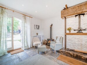 Una habitación con chimenea de piedra, un banco de madera, un sillón a rayas y vistas a través de un gran ventanal.