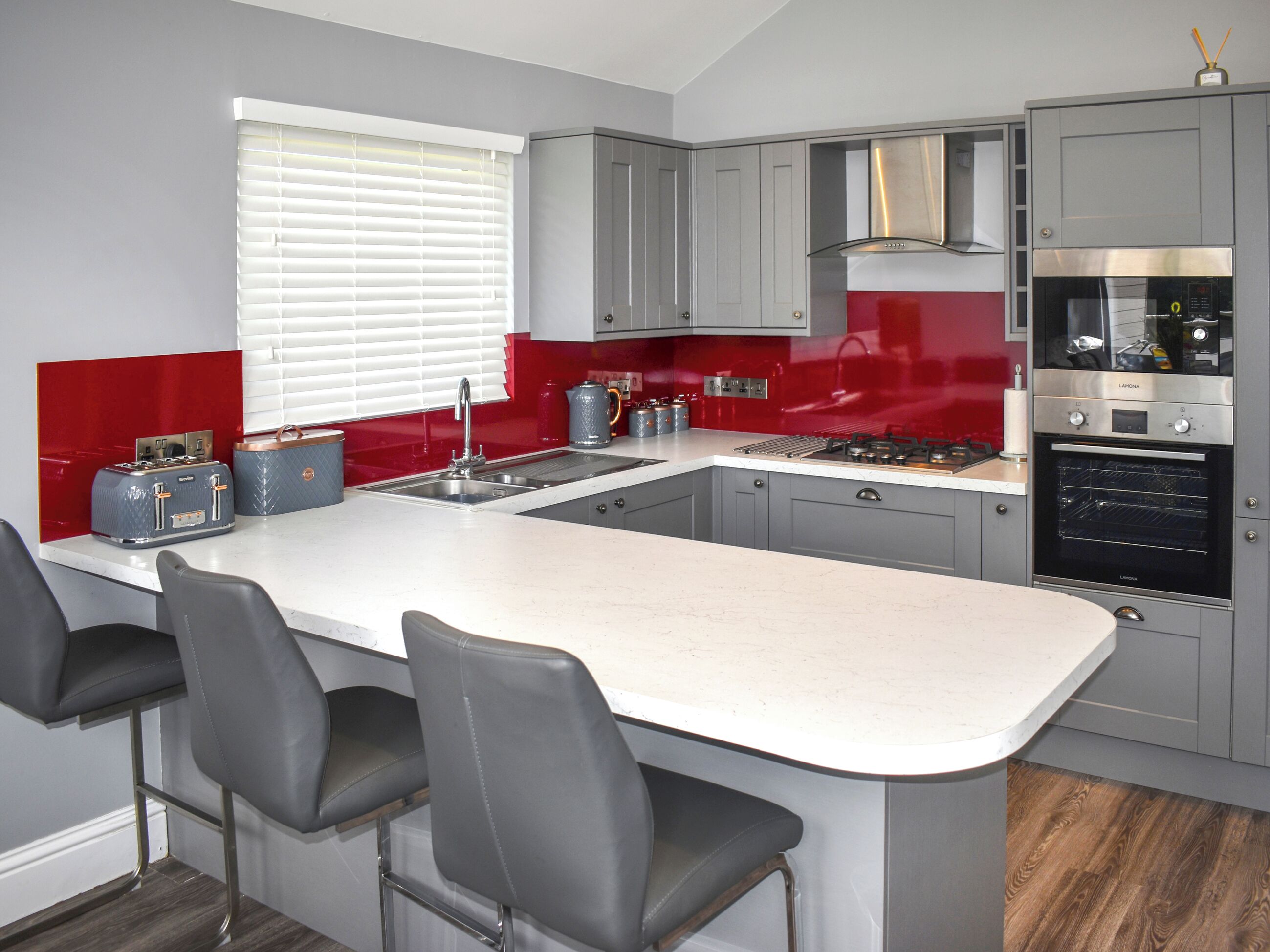A modern kitchen with grey cabinets, a white island, and a red accent wall.