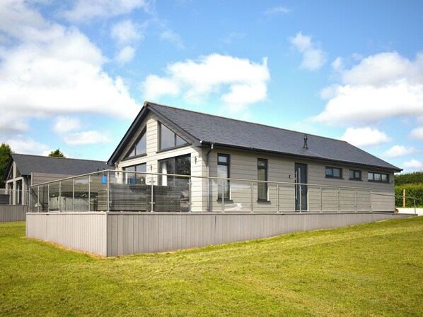 A modern building with a sloped roof, large windows, and a covered outdoor area with a railing.