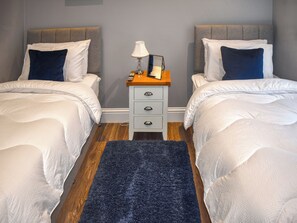 A hotel room with two beds, a nightstand with a lamp, and a dark blue rug.