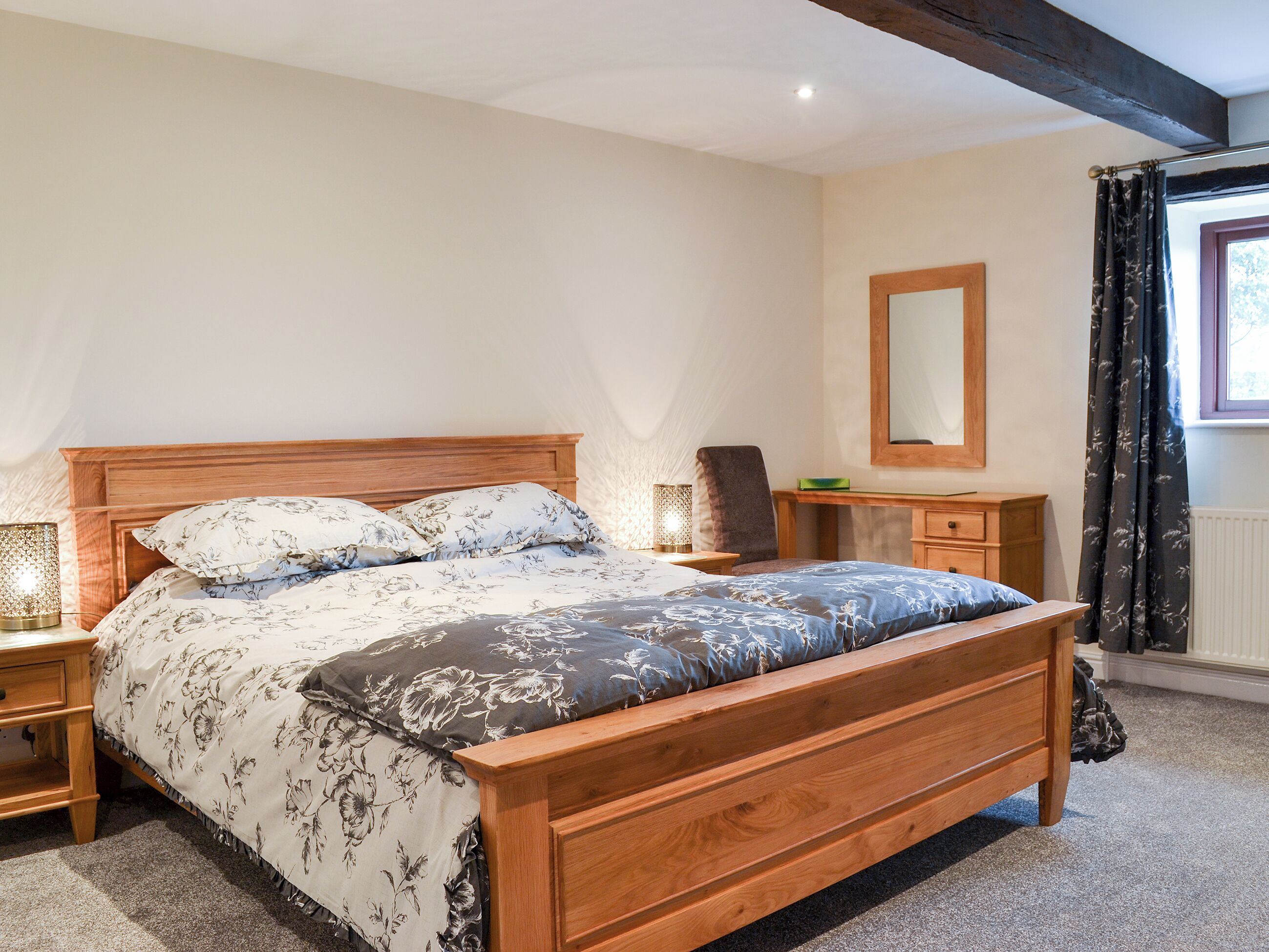 A bedroom with a wooden bed, a nightstand, a dresser, a mirror, and a window with curtains.
