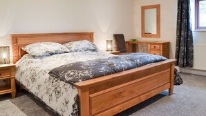 Un dormitorio con cama de madera, mesita de noche, cómoda, espejo y ventana con cortinas.