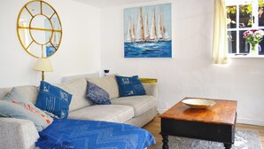 A living room with a sofa, a coffee table, a painting of sailboats, and a window with curtains. - 3 bedroom accommodation in Sidmouth (Sidmouth)