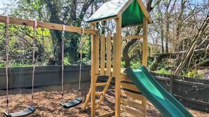 A wooden swing set with a green slide, surrounded by trees and mulch. - 3 bedroom accommodation in Sidmouth (Sidmouth)