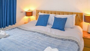 A hotel room with a bed, blue and white bedding, two bedside lamps, and a blue curtain. - 3 bedroom accommodation in Sidmouth (Sidmouth)