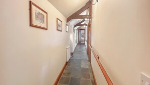 A hallway with a stone floor, wooden railing, and framed pictures on the walls.