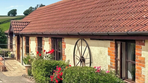 A building with a red-tiled roof, brick walls, and a large wheel visible through a window.