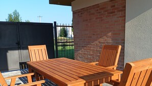 Un patio esterno in legno con tavolo e sedie, un muro in mattoni e un cancello in metallo sullo sfondo.