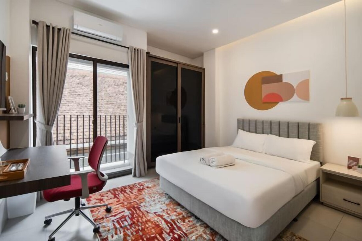 A modern hotel room with a large bed, a desk, a chair, and a view of the outside.