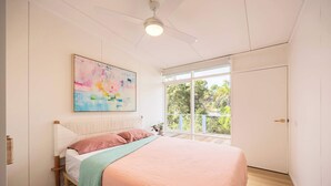 Un dormitorio con cama, ventilador de techo, ventana con vistas y un cuadro en la pared.