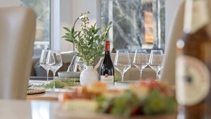 A dining table with wine glasses, a bottle of wine, and a vase with greenery. - Saltwood Coastal Hamptons Luxe with Pool (Rye)
