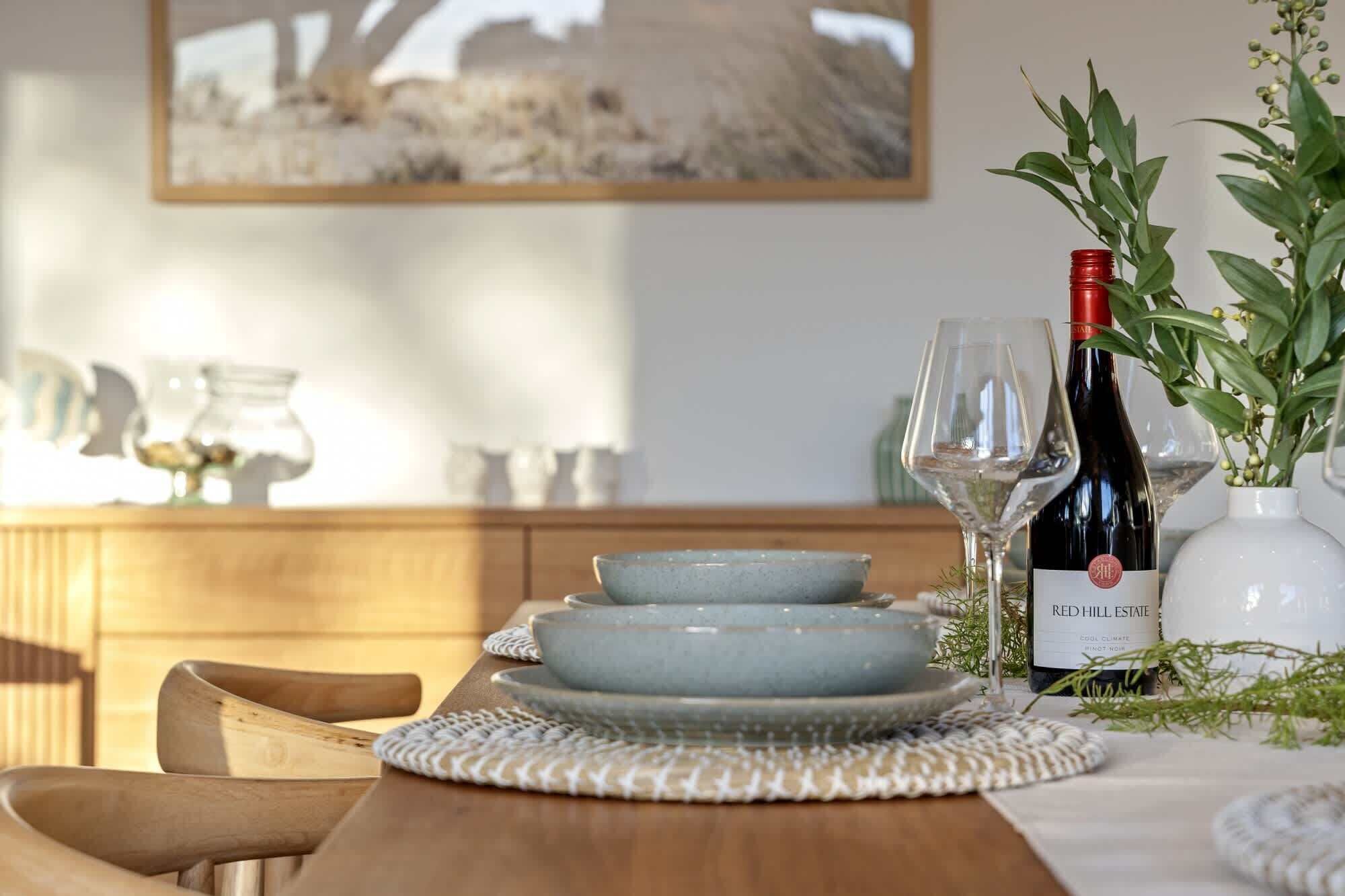 A dining table set with plates, a wine bottle, and glasses.