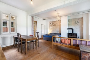 Ein Zimmer mit Esstisch aus Holz, Stühlen, einer Couch, einer Bank, einem Kamin und einer Heizung.