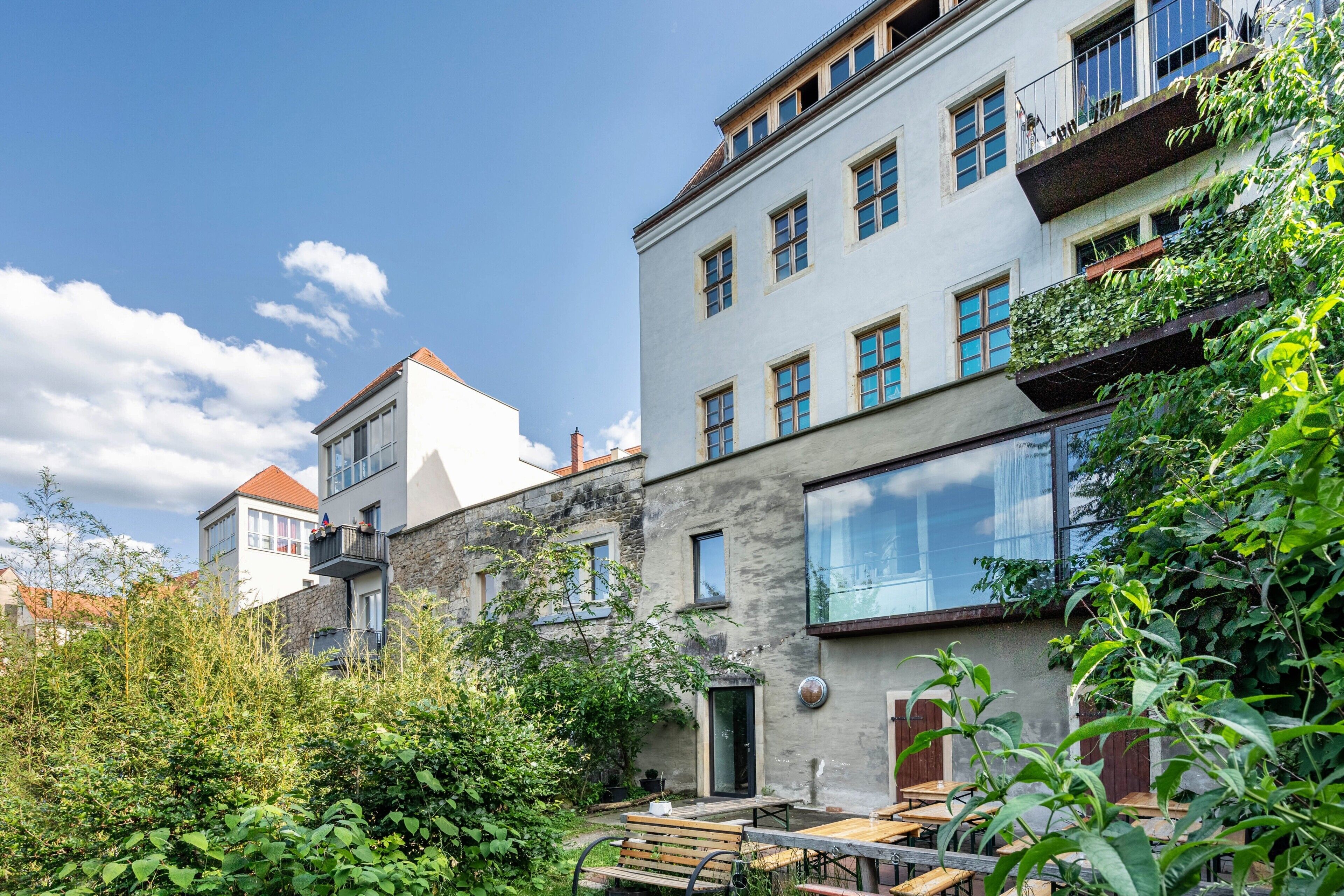 A courtyard with outdoor seating, a stone wall, and a building with multiple windows and balconies.