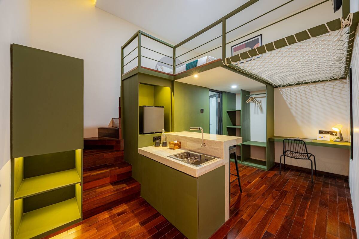 Un apartamento moderno y compacto, con kitchenette, un pequeño comedor y una escalera que lleva a un nivel superior.