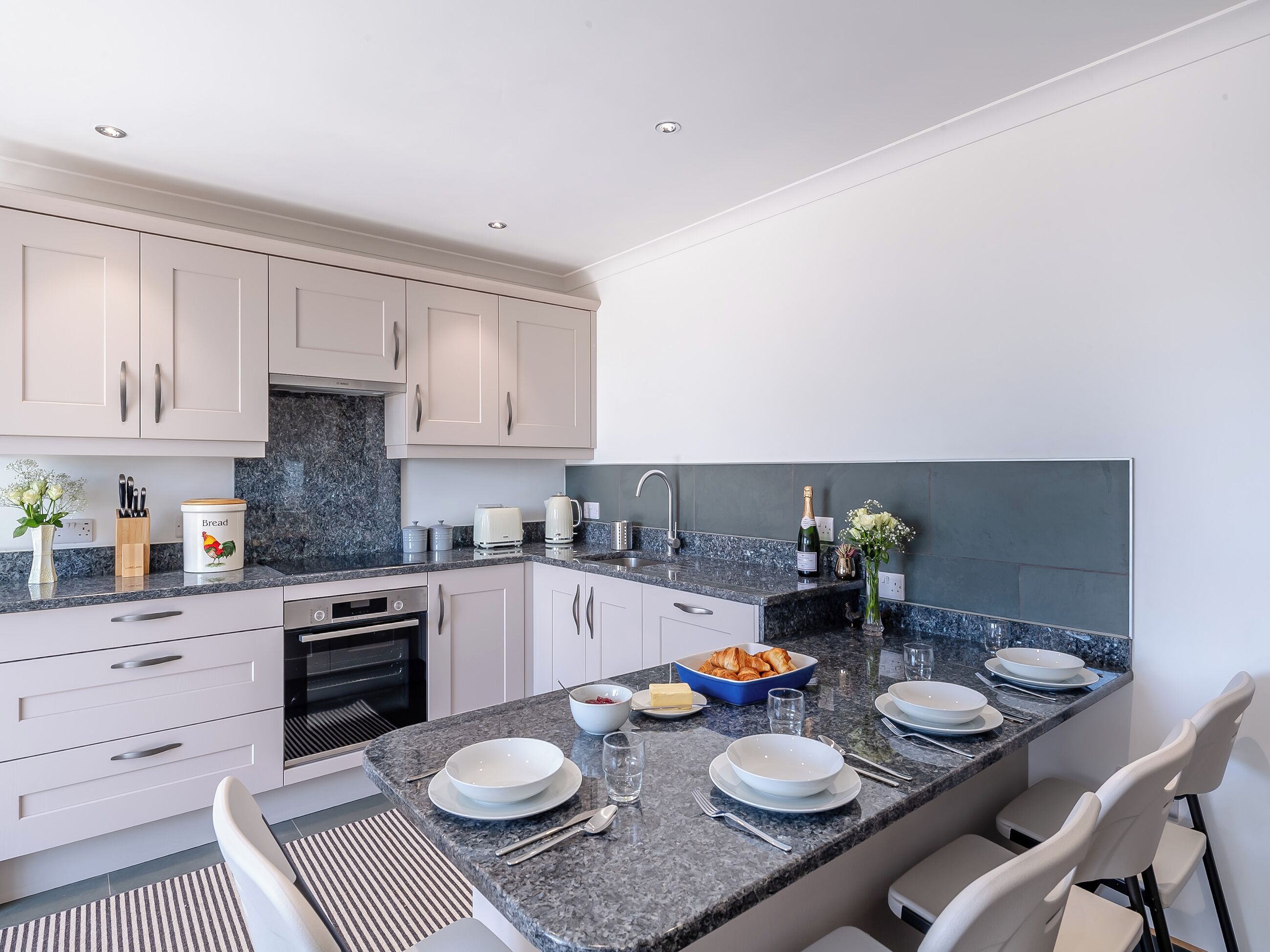 A modern kitchen with white cabinets, a granite countertop, and a built-in oven.