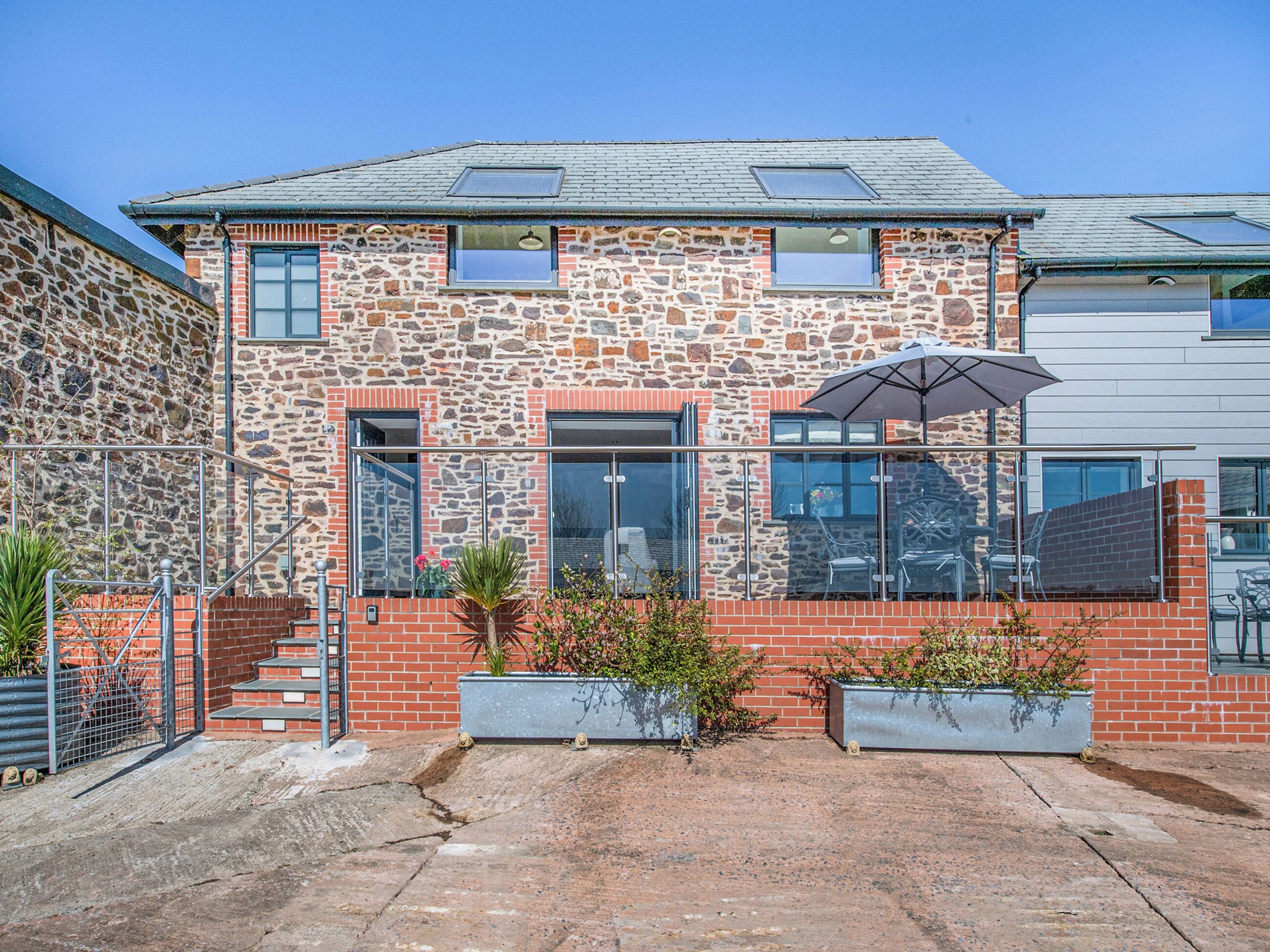 A stone and brick building with a patio area, outdoor seating, and a metal gate.