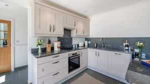 A modern kitchen with white cabinets, a granite countertop, and a built-in oven. - The Stables - UK49089 (Crediton)