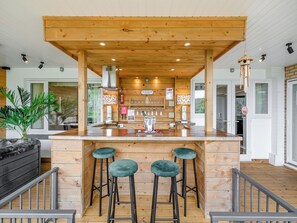 A wooden bar area with stools, a built-in sink, and a view of the outdoors.