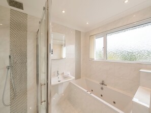 Un baño moderno con ducha de vidrio, una bañera independiente, un tocador con espejo y una ventana que proporciona luz natural.