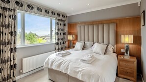Ein Schlafzimmer mit einem großen Bett, Nachttischlampen, einem Holzkopfteil und Blick durch das Fenster.