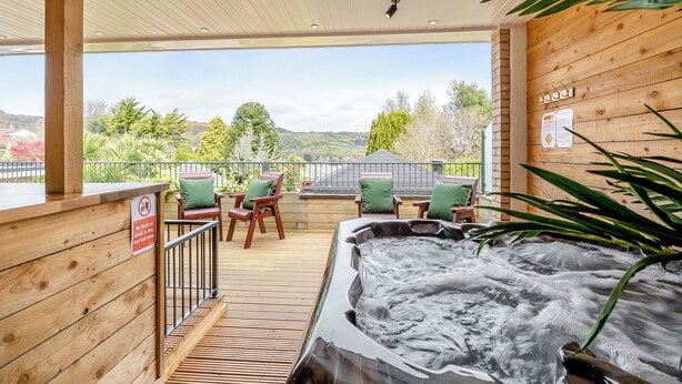 Eine Holzterrasse mit Whirlpool, Stühlen und Blick auf die Landschaft.