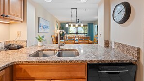 A kitchen with granite countertops, a double sink, wooden cabinets, and a dishwasher.