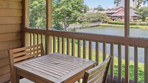 A wooden table and chairs on a balcony with a view of a lake and buildings in the background.
